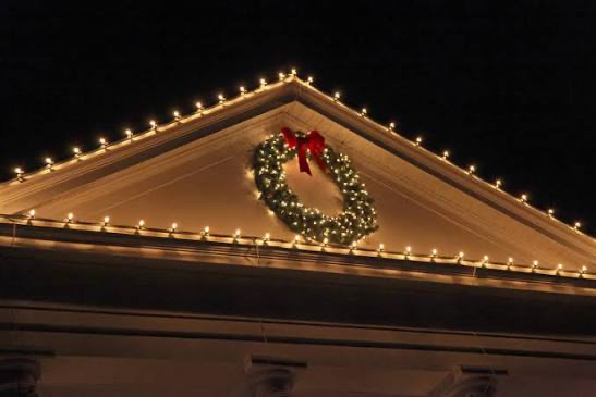 White gable peak lined with warm white lights and a pre-lit wreath with a red bow