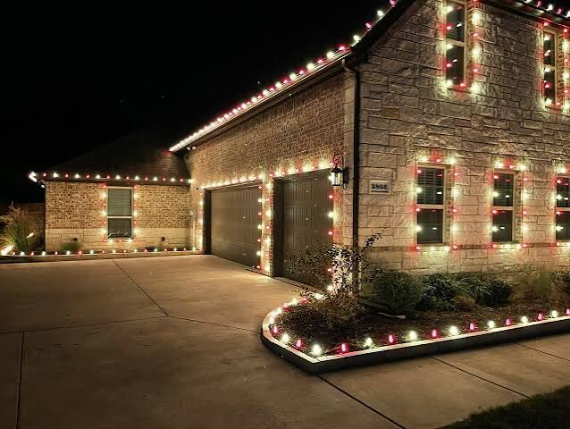 Large brick and stone home outlined in red and warm white C9 Christmas lights at night